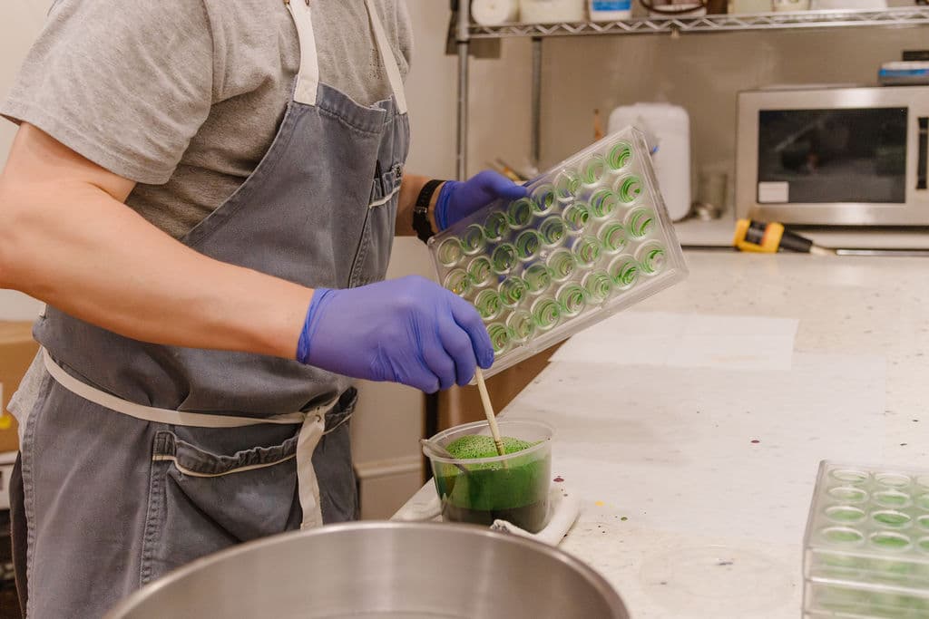 Hands in nitrile gloves tempering green pistachio chocolate into bonbon moulds