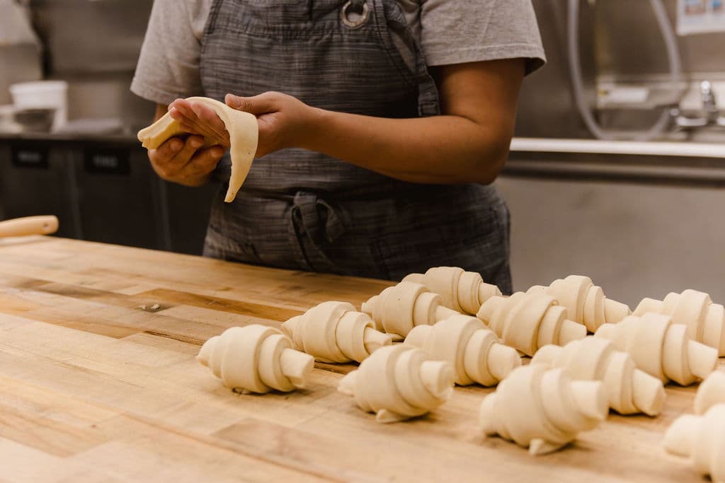 A baker shaping raw butter croissants on a wooden bench at the Edelweiss kitchen