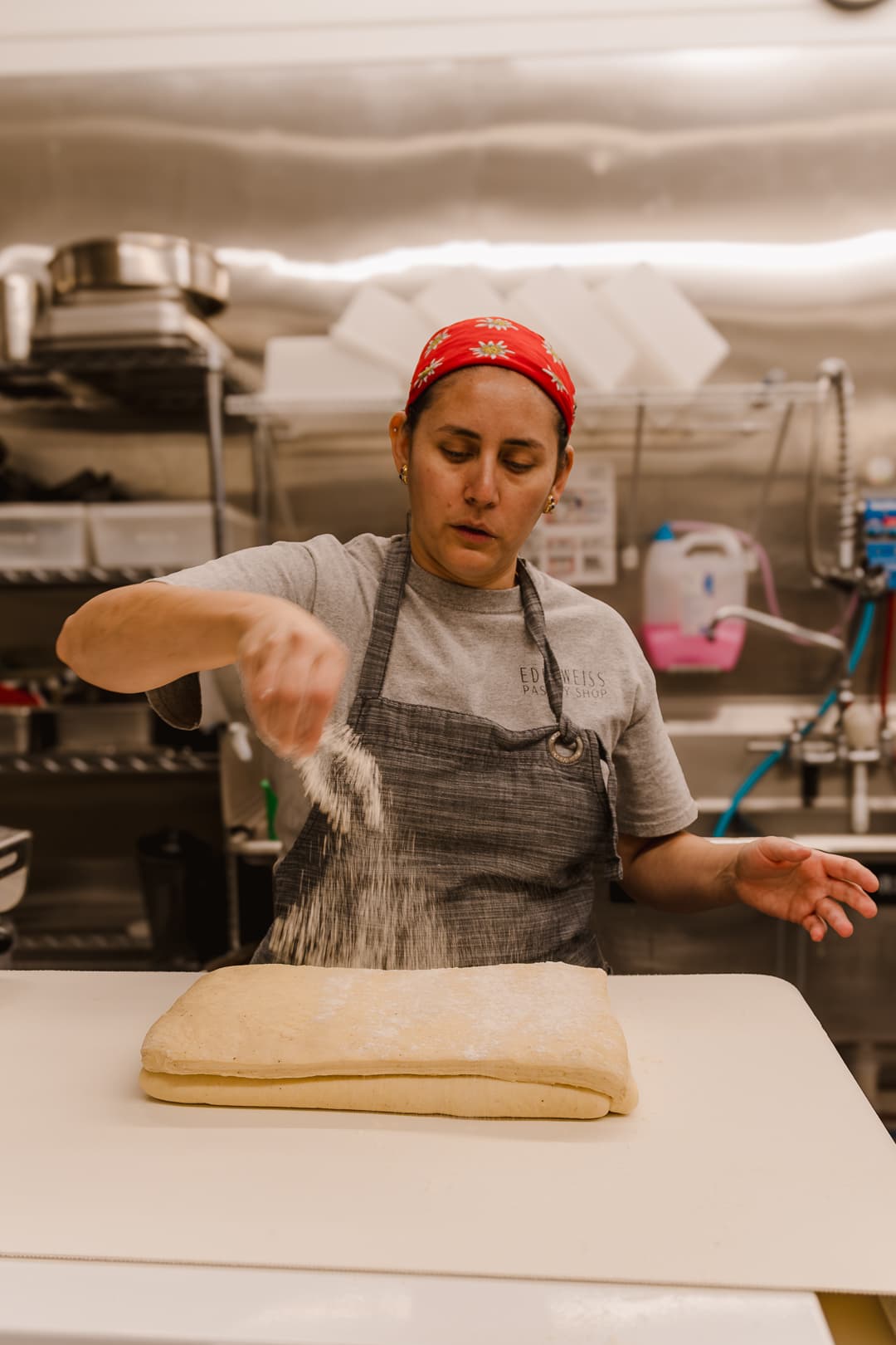 Valentina dusting flour on a sheet of laminated dough, wearing an Edelweiss apron and red edelweiss bandana